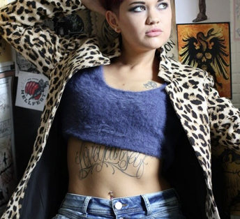 A person with a tattoo on the belly and wearing a jacket with an animal print